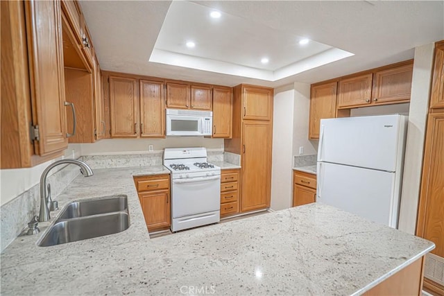 kitchen featuring white appliances, a sink, a raised ceiling, a peninsula, and recessed lighting