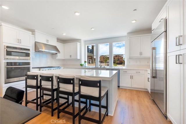 188 Merit, Irvine, CA 92618 - kitchen with under cabinet range hood, stainless steel appliances, white cabinetry, a kitchen breakfast bar, and recessed lighting