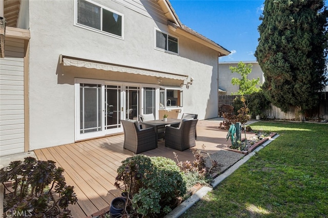 rear view of house with stucco siding, outdoor dining area, and a wooden deck