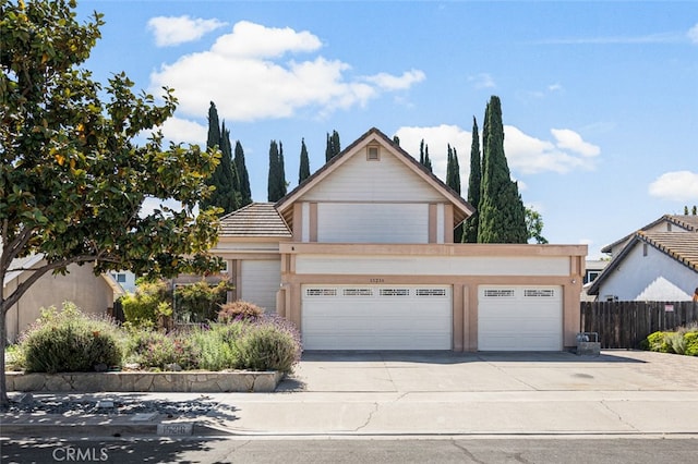 traditional home featuring a garage, concrete driveway, fence, and a tile roof