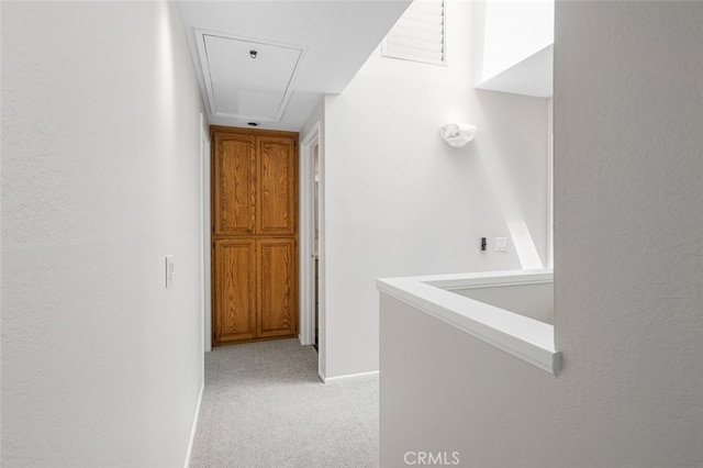hallway with attic access, light carpet, and baseboards