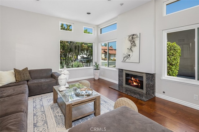living room with wood finished floors, plenty of natural light, a premium fireplace, baseboards, and a towering ceiling