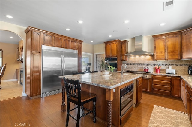 38792 Comanche Point Rd, Arvin, CA 93203 - kitchen with appliances with stainless steel finishes, wall chimney exhaust hood, arched walkways, light stone countertops, and tasteful backsplash