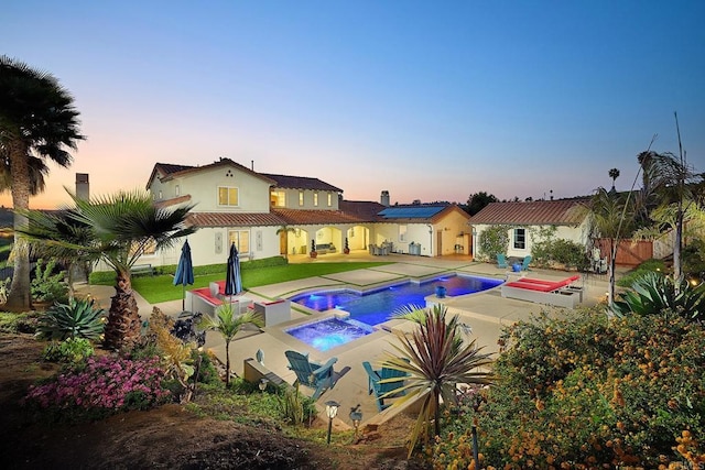 pool at dusk with a patio area and a pool with connected hot tub