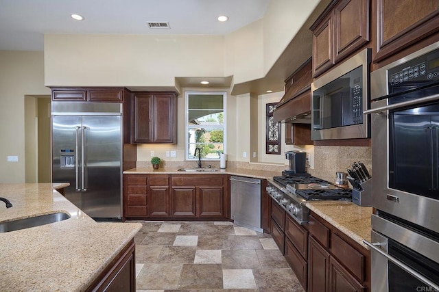 kitchen with built in appliances, a sink, light stone countertops, and recessed lighting