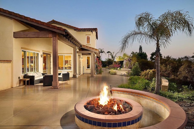 property exterior at dusk featuring stucco siding, a patio, and an outdoor living space with a fire pit