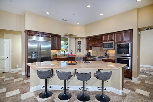 kitchen with built in appliances, premium range hood, a kitchen bar, recessed lighting, and backsplash