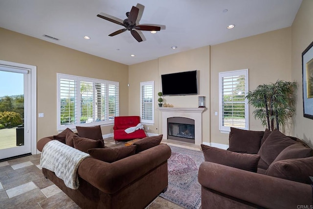 living area with plenty of natural light, a fireplace with raised hearth, recessed lighting, ceiling fan, and baseboards