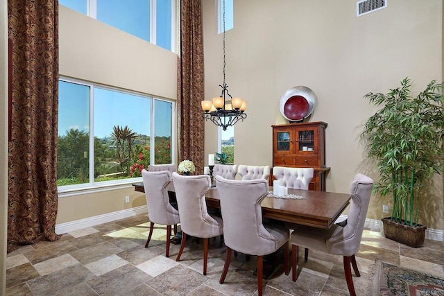 dining room with a chandelier, a towering ceiling, baseboards, and stone finish flooring
