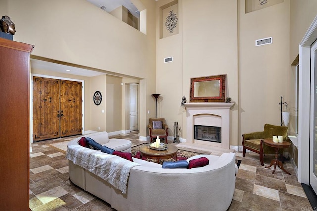 living room featuring a high ceiling, stone finish floors, a fireplace with raised hearth, and baseboards