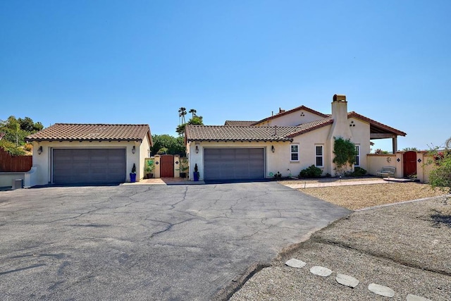 mediterranean / spanish-style home with stucco siding, a tiled roof, a gate, and a chimney
