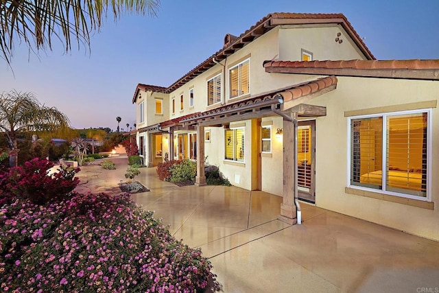 back of house at dusk featuring a patio, stucco siding, and a tiled roof