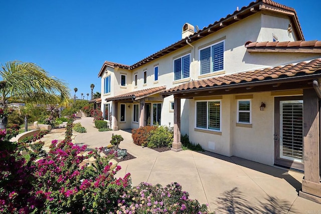 rear view of property featuring a chimney, a patio, a tile roof, and stucco siding