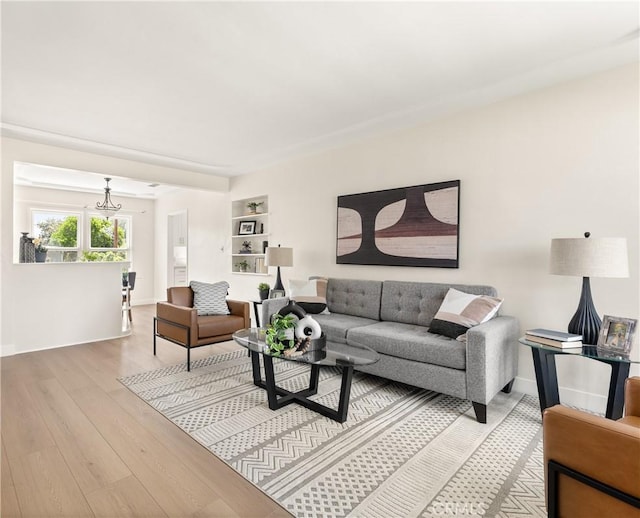 living room with light wood-style floors, a chandelier, and baseboards