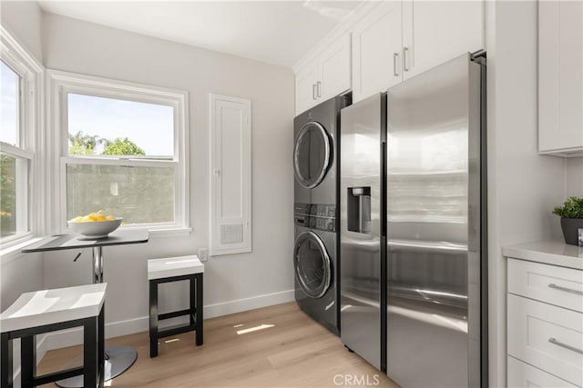 laundry room featuring stacked washing machine and dryer, light wood finished floors, and baseboards