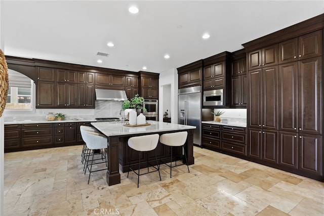 28 Dogwood, Lake Forest, CA 92630 - kitchen with built in appliances, stone tile flooring, under cabinet range hood, backsplash, and a kitchen bar
