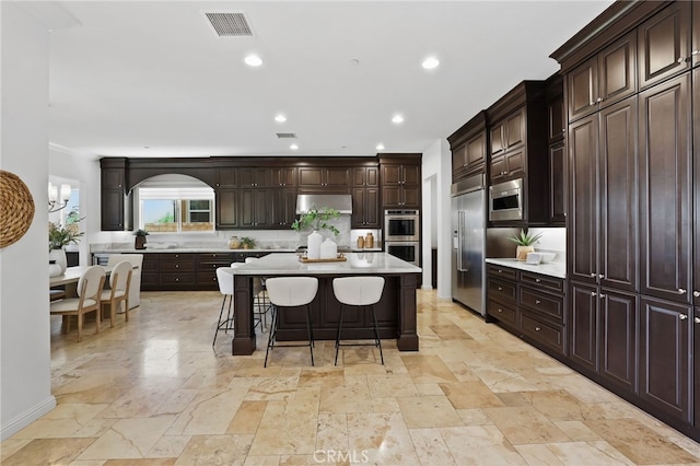 28 Dogwood, Lake Forest, CA 92630 - kitchen featuring built in appliances, under cabinet range hood, a kitchen bar, stone tile flooring, and recessed lighting