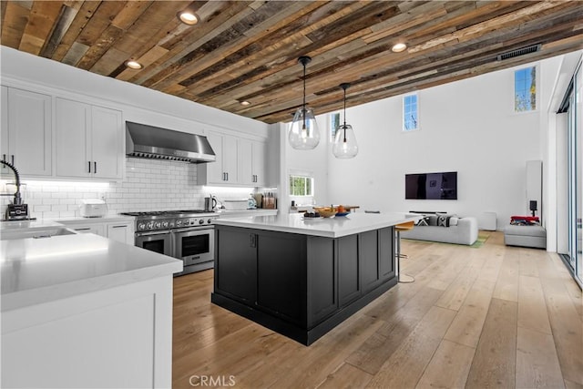 23477 Palm Dr, Calabasas, CA 91302 - kitchen featuring double oven range, wall chimney exhaust hood, white cabinetry, light countertops, and a center island