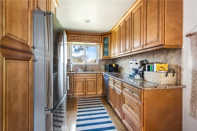 kitchen with stainless steel appliances, a sink, stone countertops, and brown cabinets