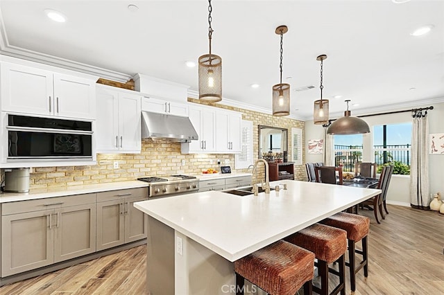 2521 Chad Zeller, Corona, CA 92882 - kitchen featuring under cabinet range hood, a sink, a kitchen breakfast bar, crown molding, and stainless steel gas cooktop