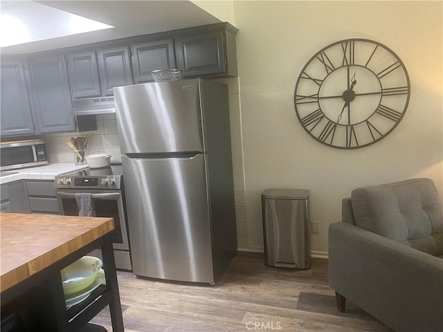kitchen with stainless steel appliances, light wood-style floors, decorative backsplash, tile counters, and under cabinet range hood