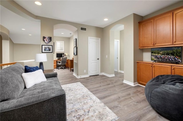 living room featuring arched walkways, light wood-style floors, a desk, baseboards, and recessed lighting