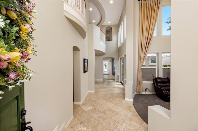hall featuring baseboards, a towering ceiling, arched walkways, recessed lighting, and stone tile floors