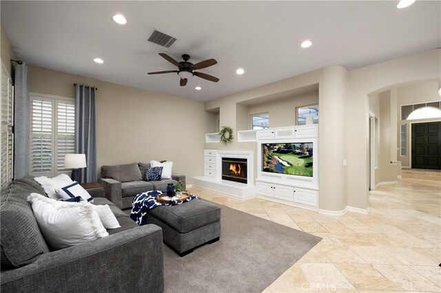 living area featuring arched walkways, recessed lighting, a ceiling fan, a glass covered fireplace, and baseboards