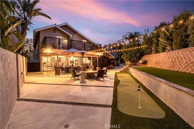 22602 Manalastas Dr, Lake Forest, CA 92630 - back of property at dusk with an area to practice putting, a balcony, a patio, an outdoor fire pit, and fence