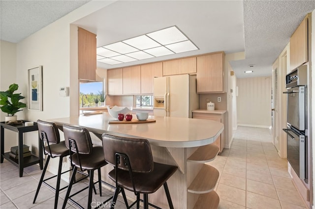 5932 Ellenview Ave, Woodland Hills, CA 91367 - kitchen featuring white refrigerator with ice dispenser, stainless steel double oven, light brown cabinets, a breakfast bar, and light tile patterned flooring