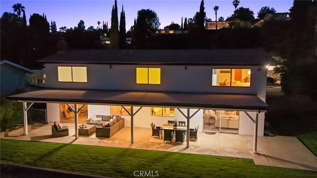 5932 Ellenview Ave, Woodland Hills, CA 91367 - back of property at dusk with an outdoor living space, a patio area, stucco siding, and a lawn