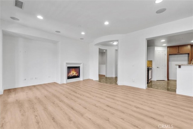 12455 Benton Dr Unit 2, Rancho Cucamonga, CA 91739 - unfurnished living room featuring light wood finished floors, recessed lighting, baseboards, a lit fireplace, and arched walkways