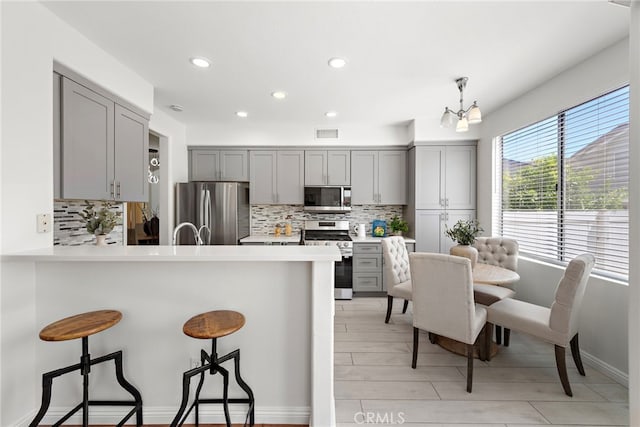 15283 Rousseau Ln, La Mirada, CA 90638 - kitchen with stainless steel appliances, gray cabinetry, a breakfast bar area, decorative backsplash, and recessed lighting