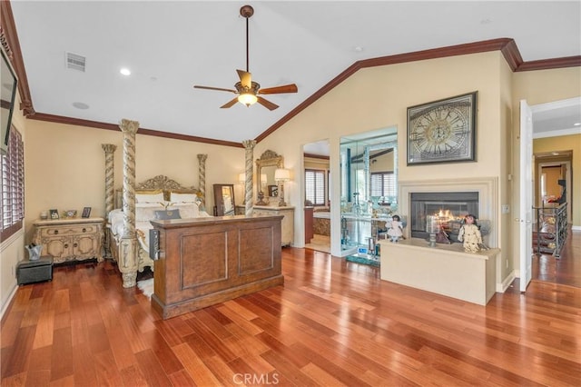 bedroom with wood finished floors, a glass covered fireplace, lofted ceiling, ornamental molding, and baseboards