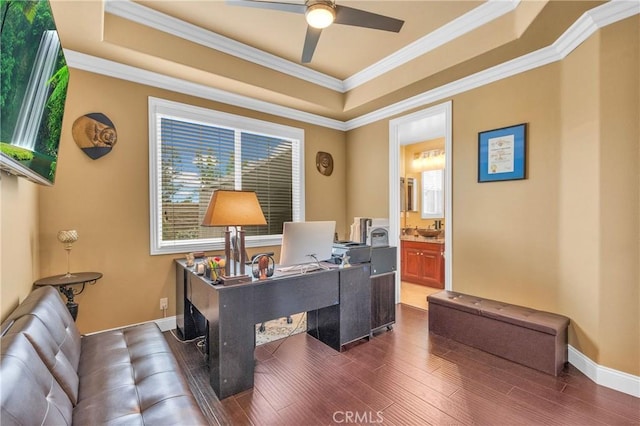 office area with a raised ceiling, a ceiling fan, dark wood-type flooring, ornamental molding, and baseboards