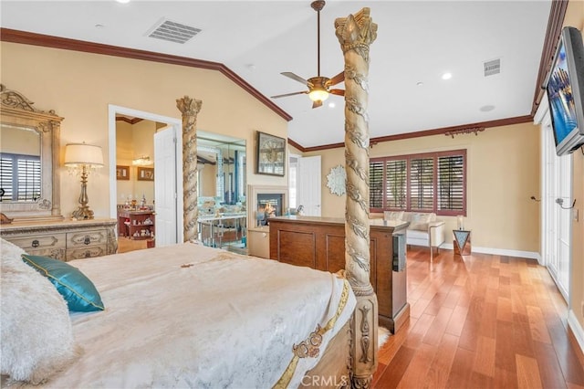 bedroom featuring ornamental molding, vaulted ceiling, multiple windows, light wood finished floors, and a glass covered fireplace