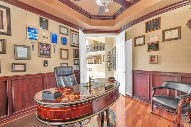 office featuring ornamental molding, wood-type flooring, a ceiling fan, a raised ceiling, and a decorative wall