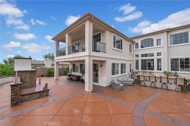 rear view of house featuring a balcony, a patio area, and stucco siding