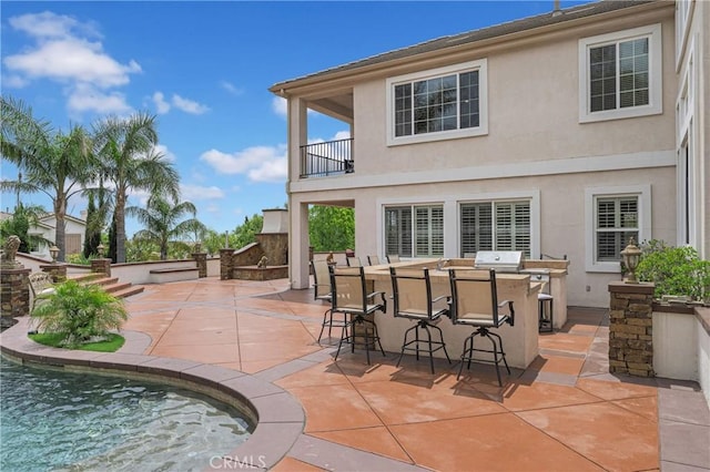 back of house with a balcony, stucco siding, a patio area, and an outdoor pool