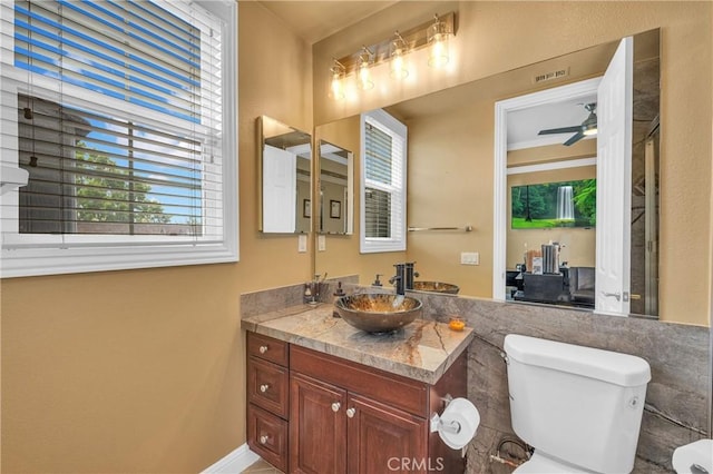 bathroom with healthy amount of natural light, toilet, vanity, tile walls, and baseboards