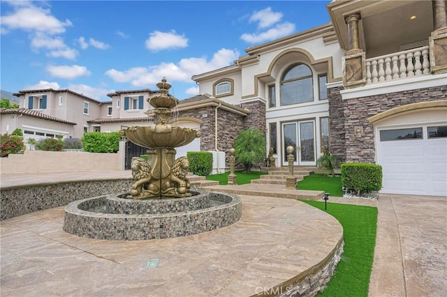 view of front of house featuring french doors, stone siding, a balcony, and stucco siding