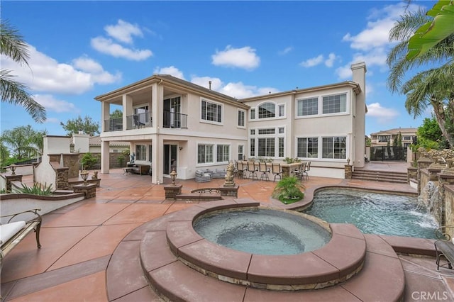 back of house with a balcony, stucco siding, a patio area, a pool with connected hot tub, and a chimney