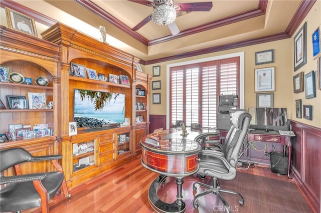 office area featuring crown molding, a ceiling fan, wainscoting, wood finished floors, and a decorative wall