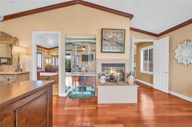 living room with wood finished floors, a multi sided fireplace, baseboards, crown molding, and vaulted ceiling