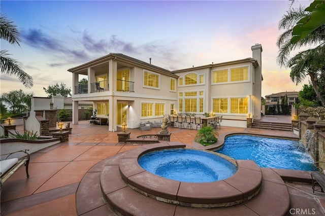 back of house with a balcony, a patio area, stucco siding, and a pool with connected hot tub