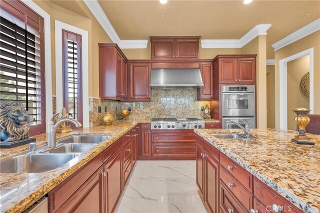 kitchen featuring appliances with stainless steel finishes, a sink, wall chimney range hood, light marble finish flooring, and crown molding