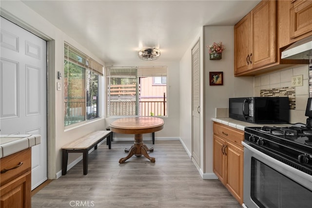 21964 Mojave River Rd, Cedarpines Park, CA 92322 - kitchen featuring gas stove, black microwave, backsplash, tile counters, and light wood finished floors