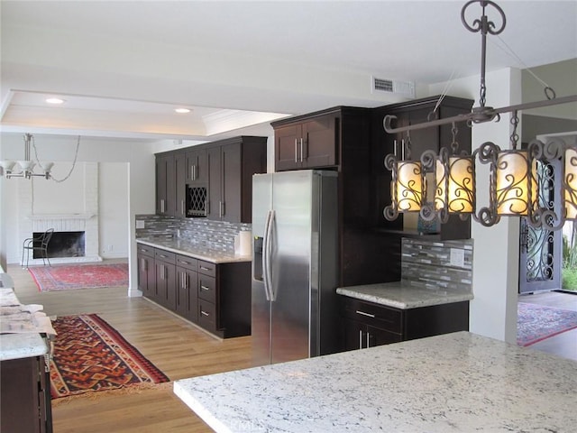 26925 Via Grande, Mission Viejo, CA 92691 - kitchen with stainless steel fridge, tasteful backsplash, light wood-style flooring, a brick fireplace, and light stone countertops