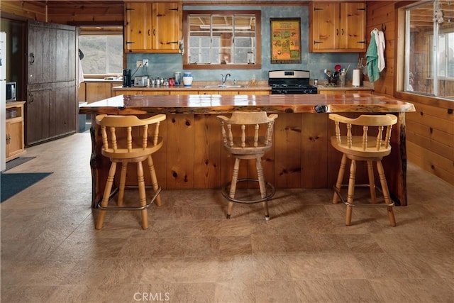 9000 Figueroa Mountain Rd, Los Olivos, CA 93441 - kitchen with stainless steel gas stove, brown cabinets, a sink, light floors, and wood walls