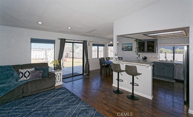 kitchen with a sink, a breakfast bar area, dark wood-style flooring, a peninsula, and dishwasher